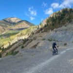 Mountain biker ascends gravel path into mountains.
