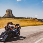 two people on motorcycle ride past devils tower