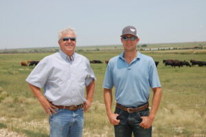 Two men stand in front a herd of cattle in a grassland