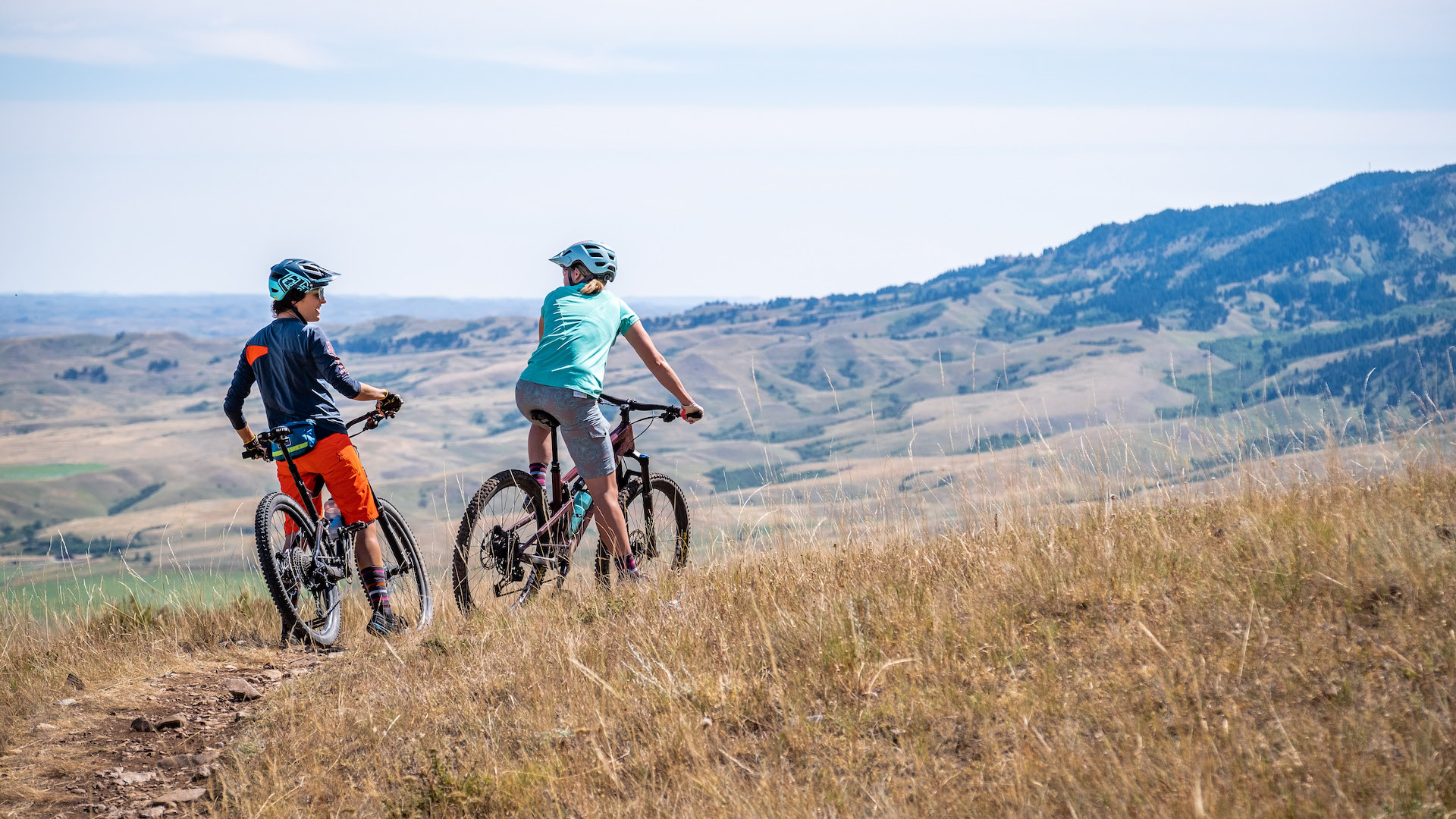 Two women riding mountain bikes through grassy foothills.