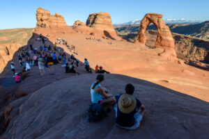 A hillside of hikers view Delicate Arch in Arches National Park outside of Moab
