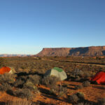 A bunch of tents pitched in the desert with red rock buttes on the horizon