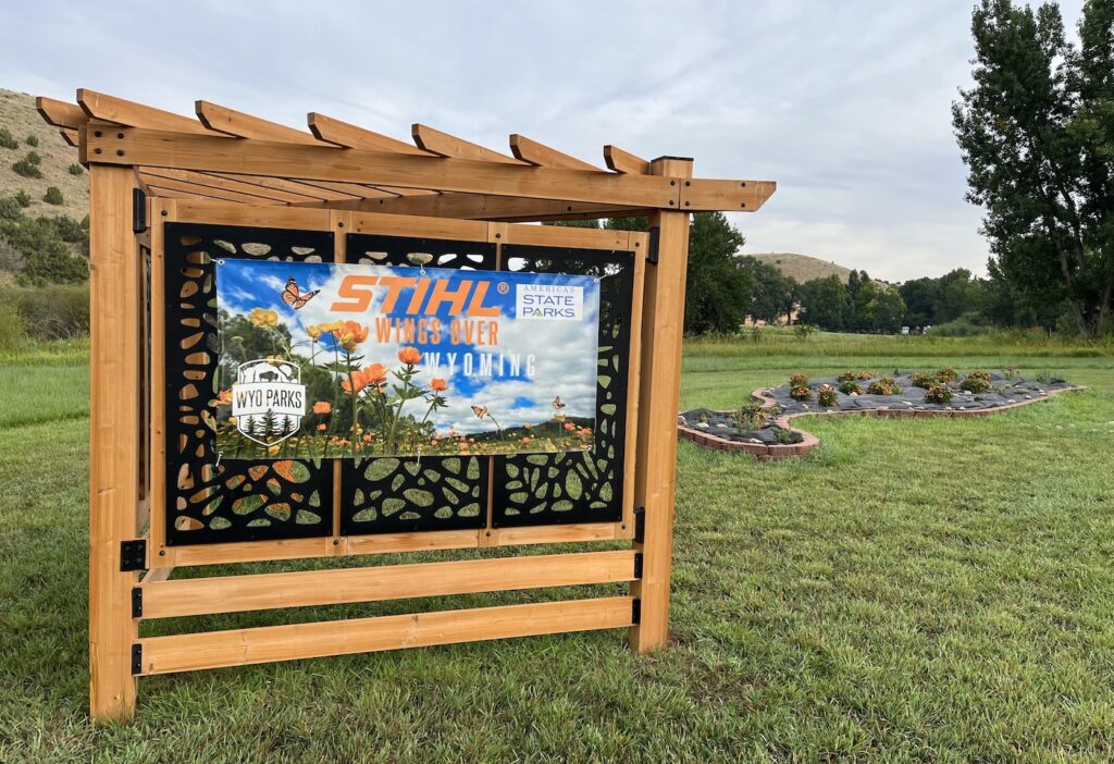 Photo of a sign reading "STIHL Wings Over Wyoming, Wyo State Parks" in front of a pollinator garden.