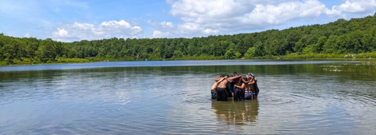 Photo of students standing in a lake with their arms around one another.