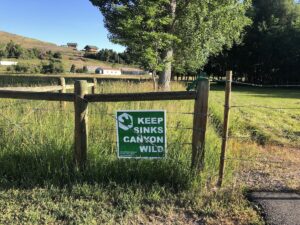 A sign reading "Keep Sinks Canyon Wild" attached to a fence. 