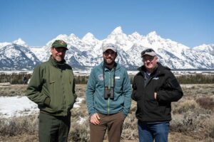 Grand Teton National Park Superintendant Chip Jenkins, EcoTour Adventures Owner Taylor Phillips, and Wyoming Game andFish Director Brian Nesvik pose in front of a snowy Teton ridge line. 