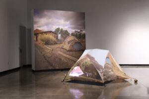 A tent with scenes of Arches National Park is set up in a gallery in front of a photo of the tent set up in Arche. 