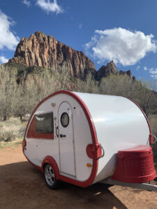 A small teardrop trailer parked in front of a red sandstone butte